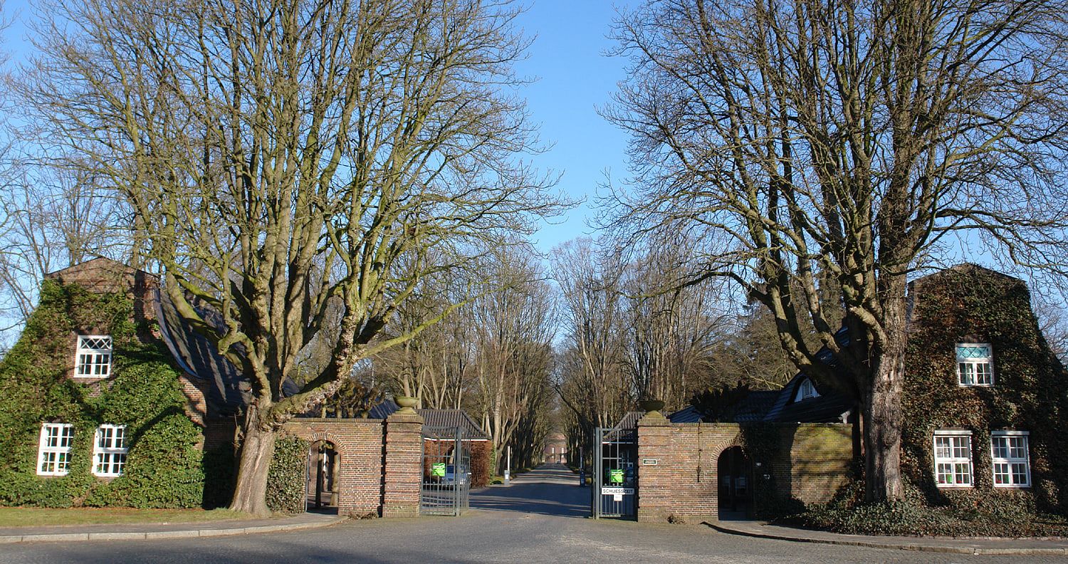 Haupteingang zwischen zwei Backsteingebäuden und mächtigen laublosen Bäumen auf Osterholzer Friedhof