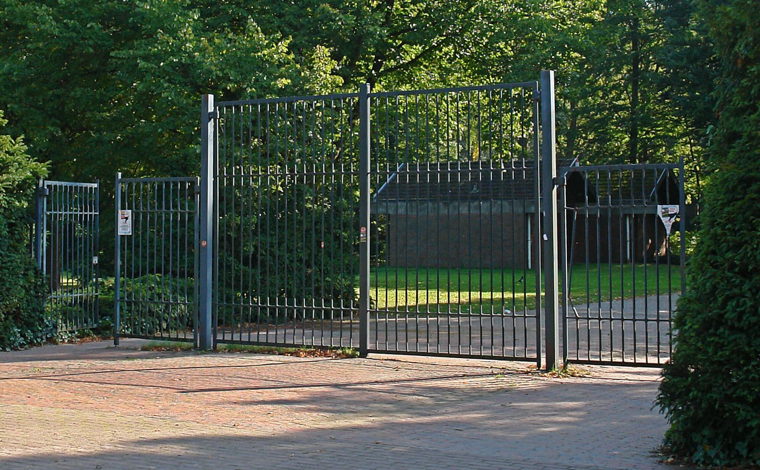 Hohes Metalltor in schräger Ansicht mit einem niedrigen dunklen Gebäude dahinter auf Osterholzer Friedhof