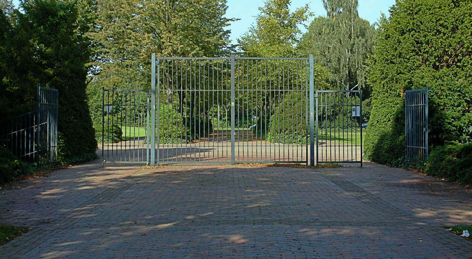 Frontalansicht eines hohen Metalltors zwischen geschnittenen Hecken auf Osterholzer Friedhof