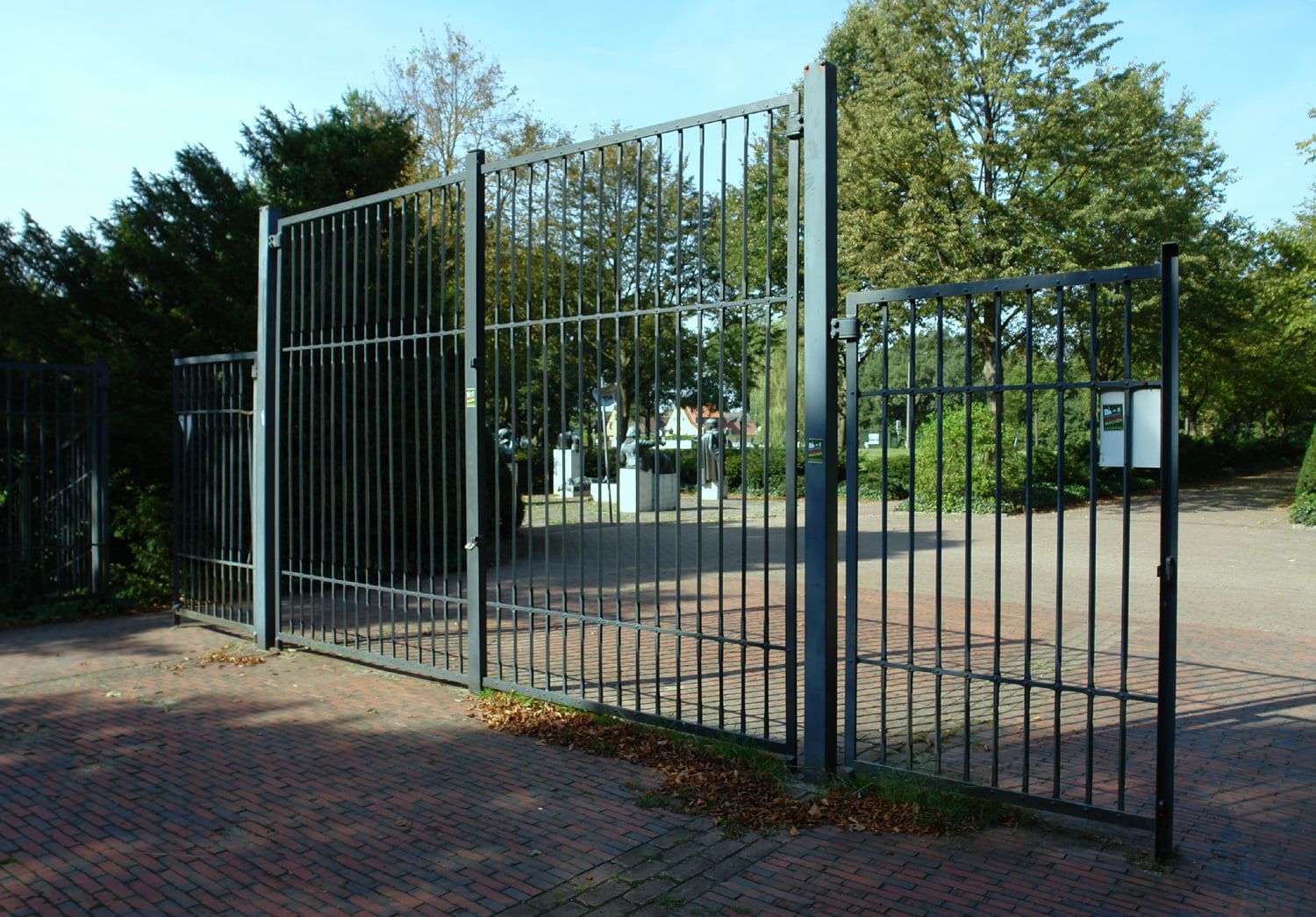 Geöffnetes Metalltor mit gepflasterten Wegen und einem Denkmal im Hintergrund auf Osterholzer Friedhof